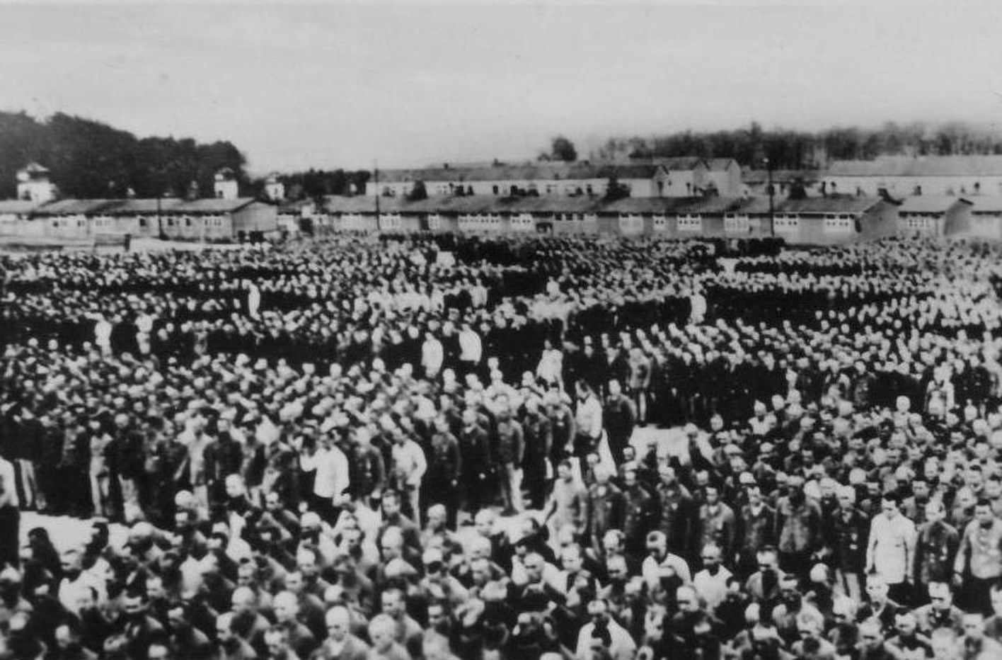Zum Appell angetretene, blockweise aufgestellte, Häftlinge des Konzentrationslagers Buchenwald. Es handelt sich um tausende. Einzelne Gesichter sind kaum zu erkennen Im Hintergrund die Lagerbaracken. 
