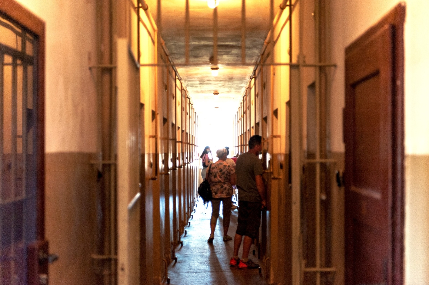 View into the cross corridor of the detention cell building. Individual visitors stand in front of various cells and look inside.