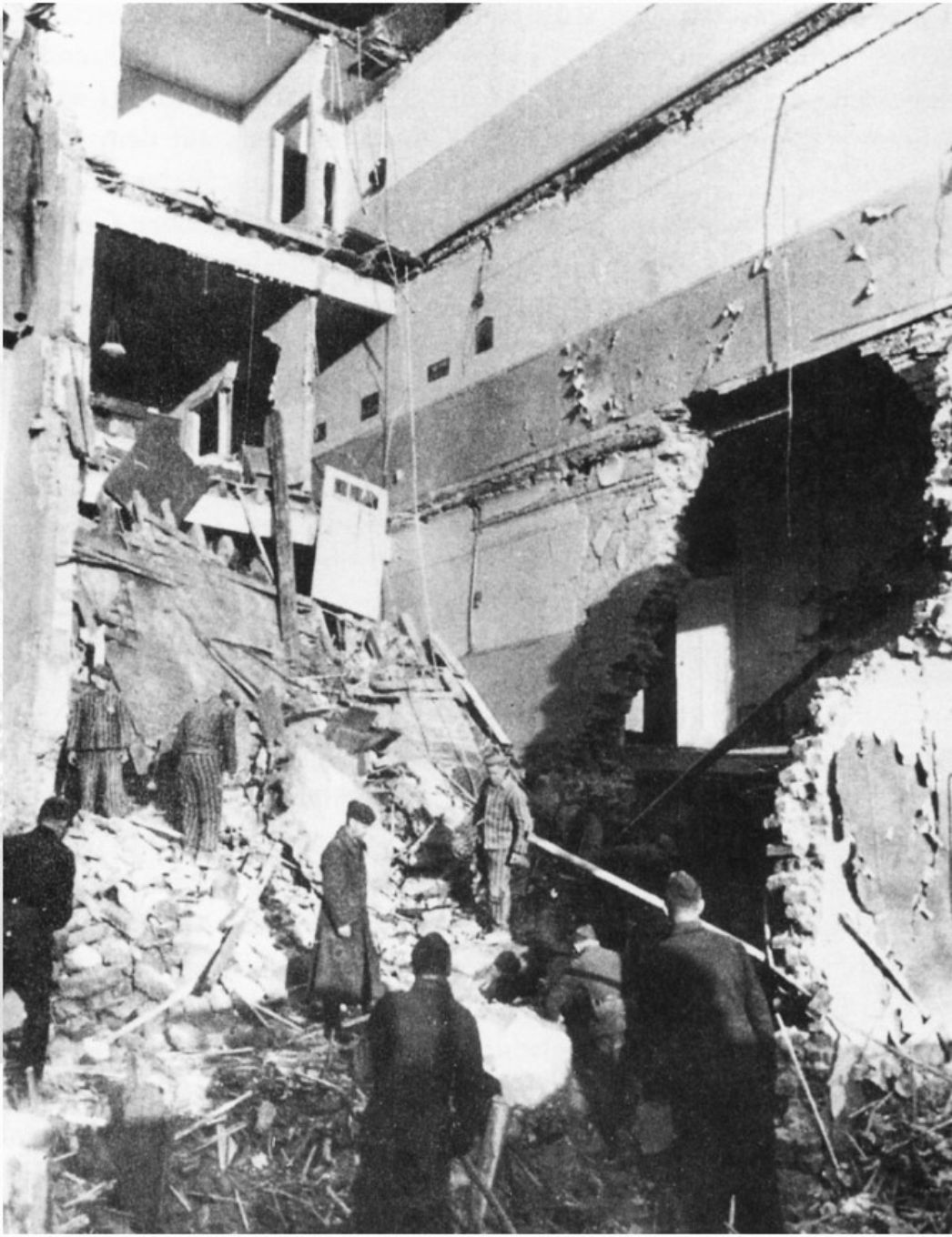 KZ-Häftlinge bei Aufräumarbeiten nach dem Bombenangriff. Zu sehen sind Mehrere Männer in Häftlingskleidung die Schutt und Trümmer aus einem zerbombten Gebäude schaufeln.