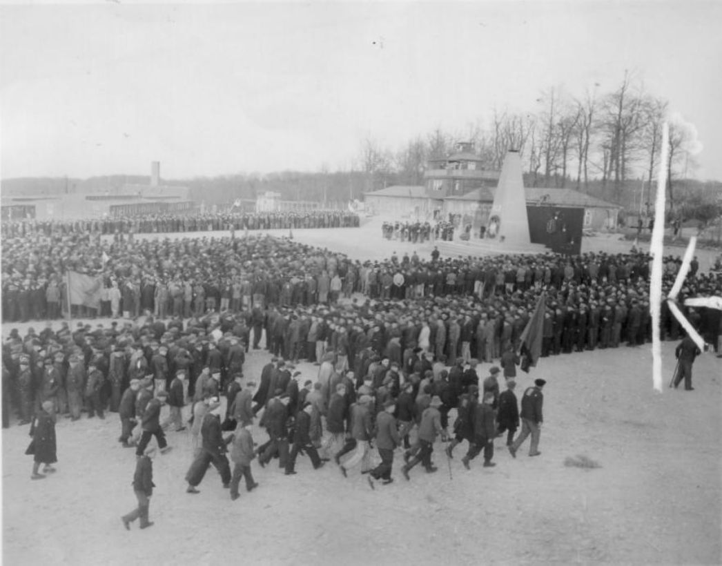 Befreite Häftlinge bei der ersten Gedenkfeier für die Toten des KZ Buchenwald. Im Hintergrund ist das provisorische Mahnmal für die Toten zu sehen.