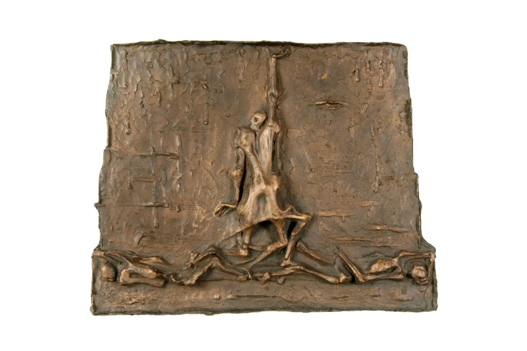 The bronze relief shows a prisoner rising among emaciated corpses.