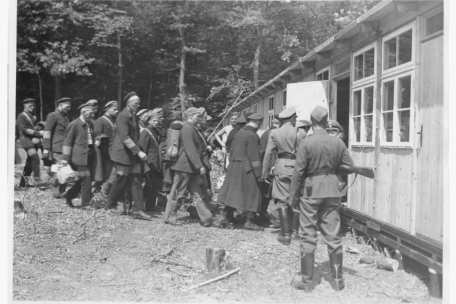 Die ersten Häftlinge werden von SS-Männern in eine Baracke greführt.
