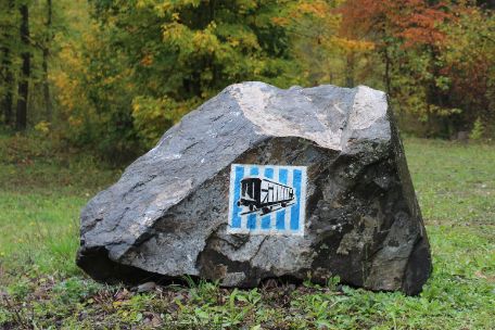 Stein, auf dem das Zeichen des Gedenkweges Buchenwald aufgesprüht ist.