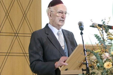 Alfred Salomon at the inauguration of the new synagogue in Bochum. He is standing at a lectern decorated with flowers and a microphone. He is wearing a black suit and a black kippah.