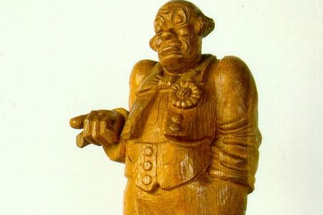 A photo of a wooden sculpture of a clown, whose gestures and facial expression make an indifferent impression.