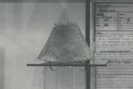 Zusehen ist ein kleiner Lampenschirm aus Menschenhaut der an einer Austellungswand präsentiert wird.