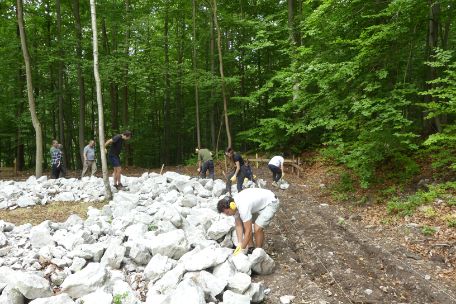 Junge Freiwillige positionieren weißlichen Bruchstein, um mit ihm die Umrisse eines ehemaligen Lagergebäudes sichtbar zu machen.