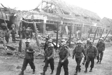 Seven American soldiers on the road in front of the destroyed vehicle garages of the satellite camp Boelcke-Kaserne. 