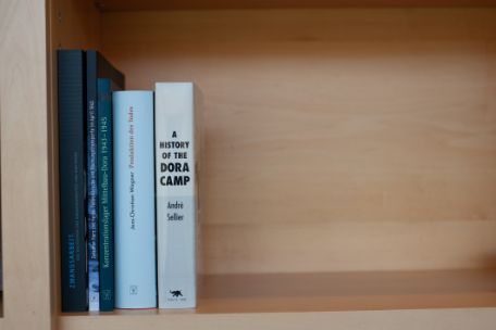 Es stehen fünf Bücher nebeneinander aufrecht in einem Regal.