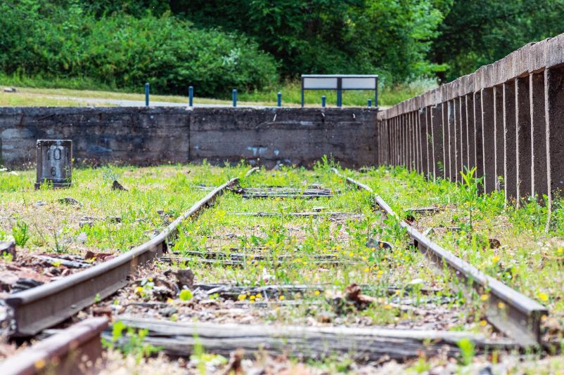 Frog perspective from the track bed. The rails to the right of the high platform are bent. Grasses are sticking out between them. A milestone of the Buchenwaldbahn can be seen on the left.Frog perspective from the track bed. The rails to the right of the high platform are bent. Grasses are sticking Frog perspective from the track bed. The rails to the right of the high platform are bent. Grasses are sticking out between them. A milestone of the Buchenwaldbahn can be seen on the left.between them. A milestone of the Buchenwaldbahn can be seen on the left.