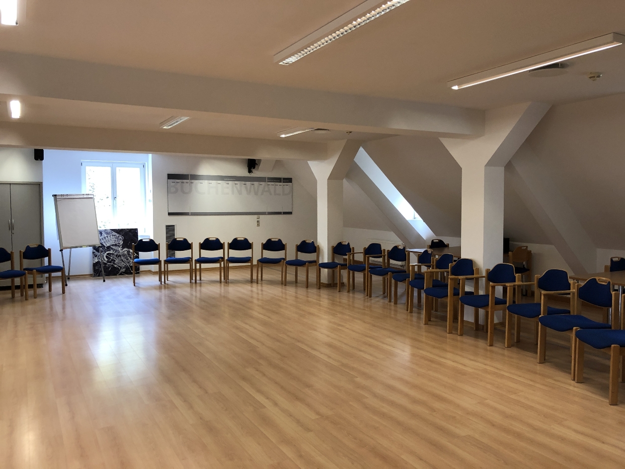 View into a seminar room of the International Youth Meeting Center. There are chairs in a semicircle. In the background, a timeline can be seen on the wall. A flipchart is in front of the window.