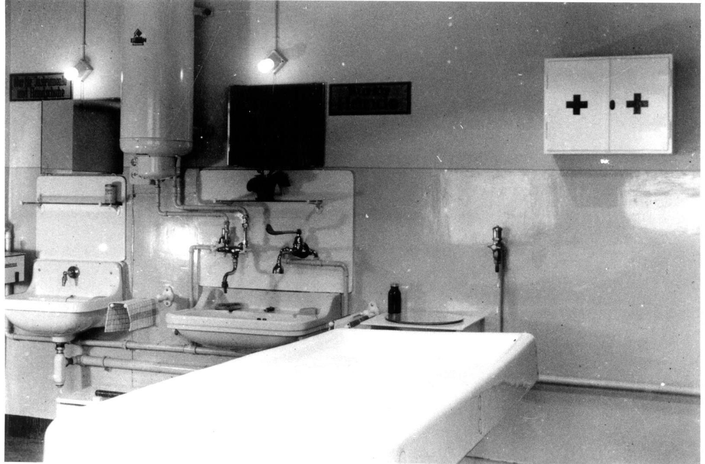 Dissection room of the pathology department in the annex of the crematorium. Center: Dissecting table. Left: Wash basin. Right on the wall: medicine cabinet with red cross.