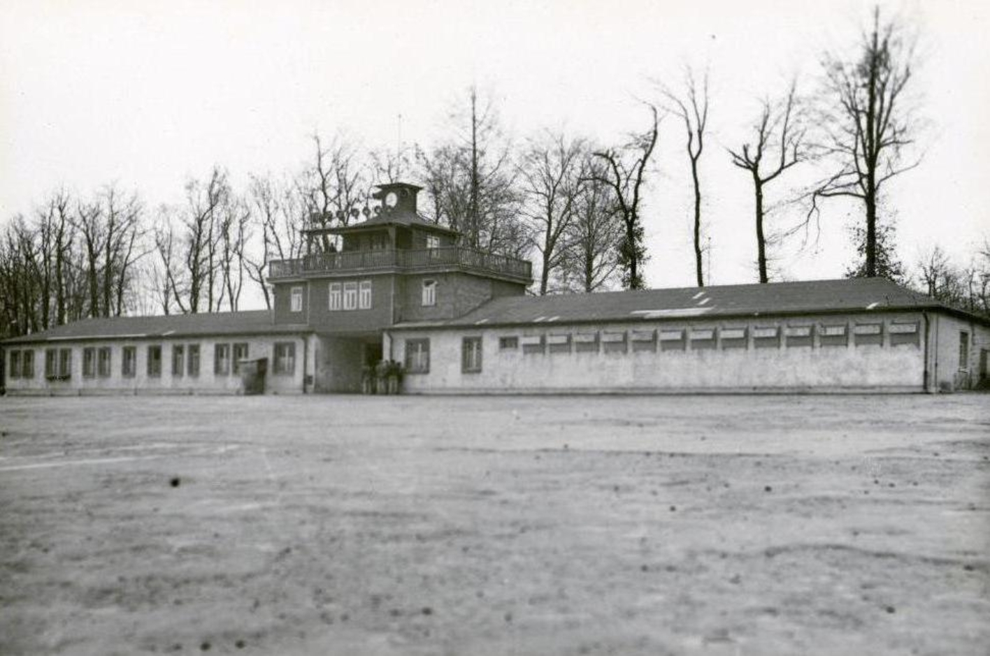 View across the empty roll call square to the gate building. The window panes of the detention cell building can be seen on the right annex.