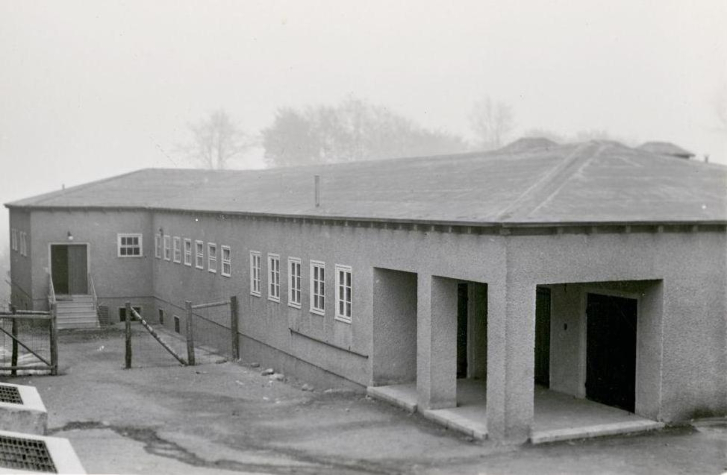 The disinfection building from the outside. A simple, flat building. Two entrances can be seen. A smaller one on the left behind a fence, one on the right in front.