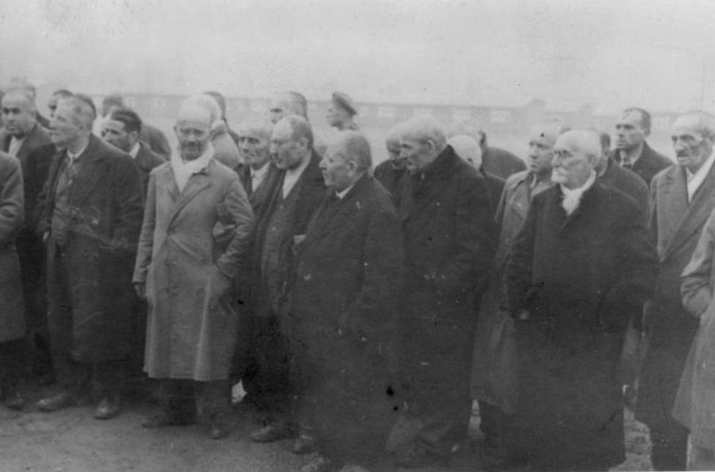 Eine Gruppe polnischer Häftlinge in Zivilkleidung steht auf dem Appellplatz. Es handelt sich vorwiegend um ältere Männer. Foto von vorne mitte Rechts.