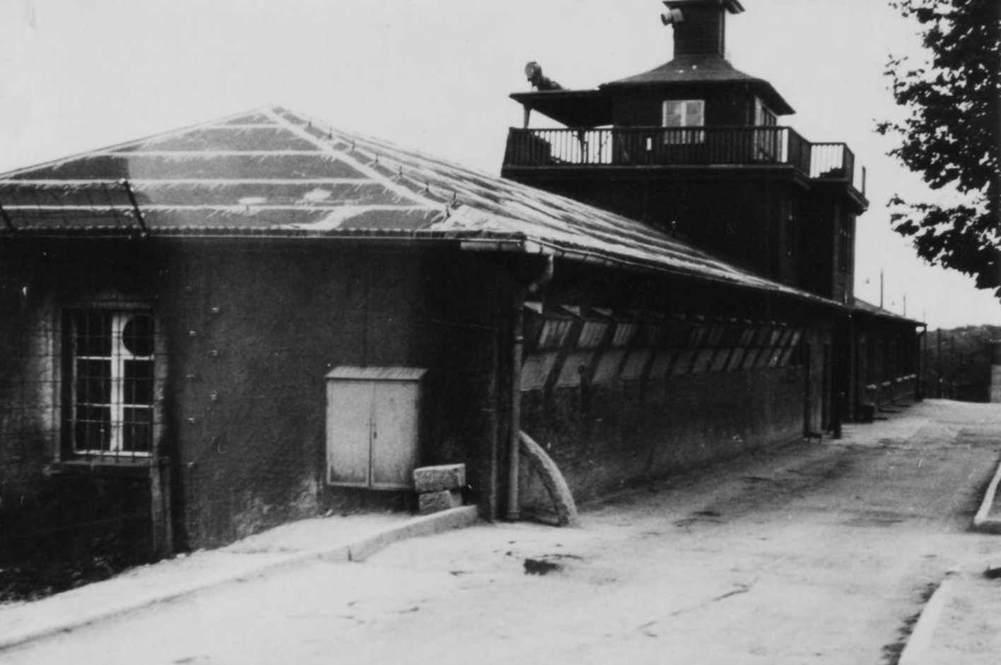 In front on the left is the detention cell building in the right wing of the gate building. In the center is the main watchtower above the camp gate. Behind it is the left wing of the gate building.