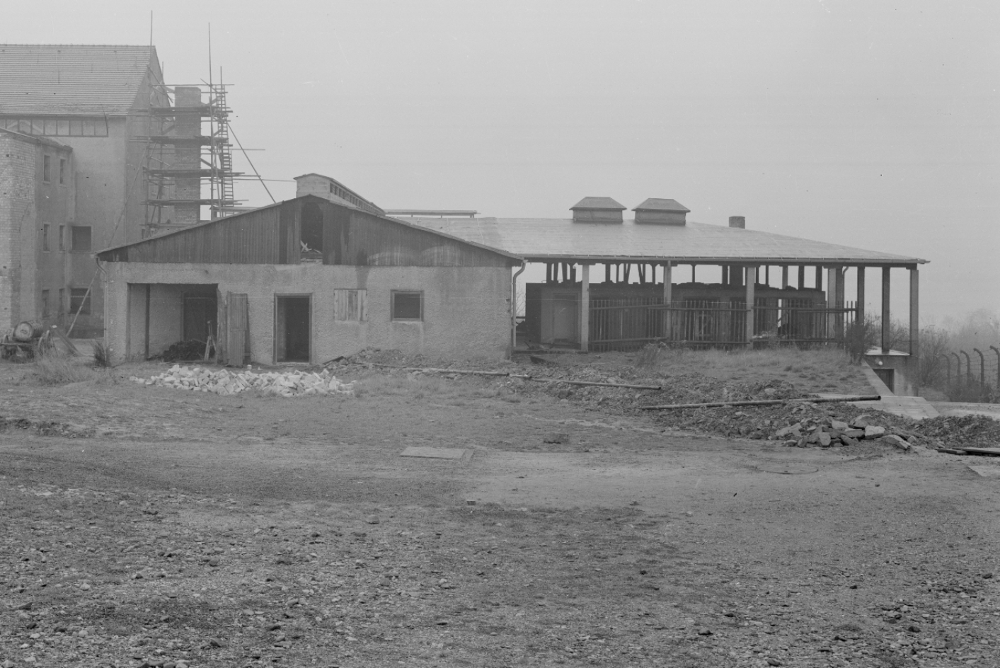 The front view of the disinfection building can be seen. The flat building is open. The chimney is scaffolded and is being dismantled. The right part of the building has no exterior walls at the time of the photo.