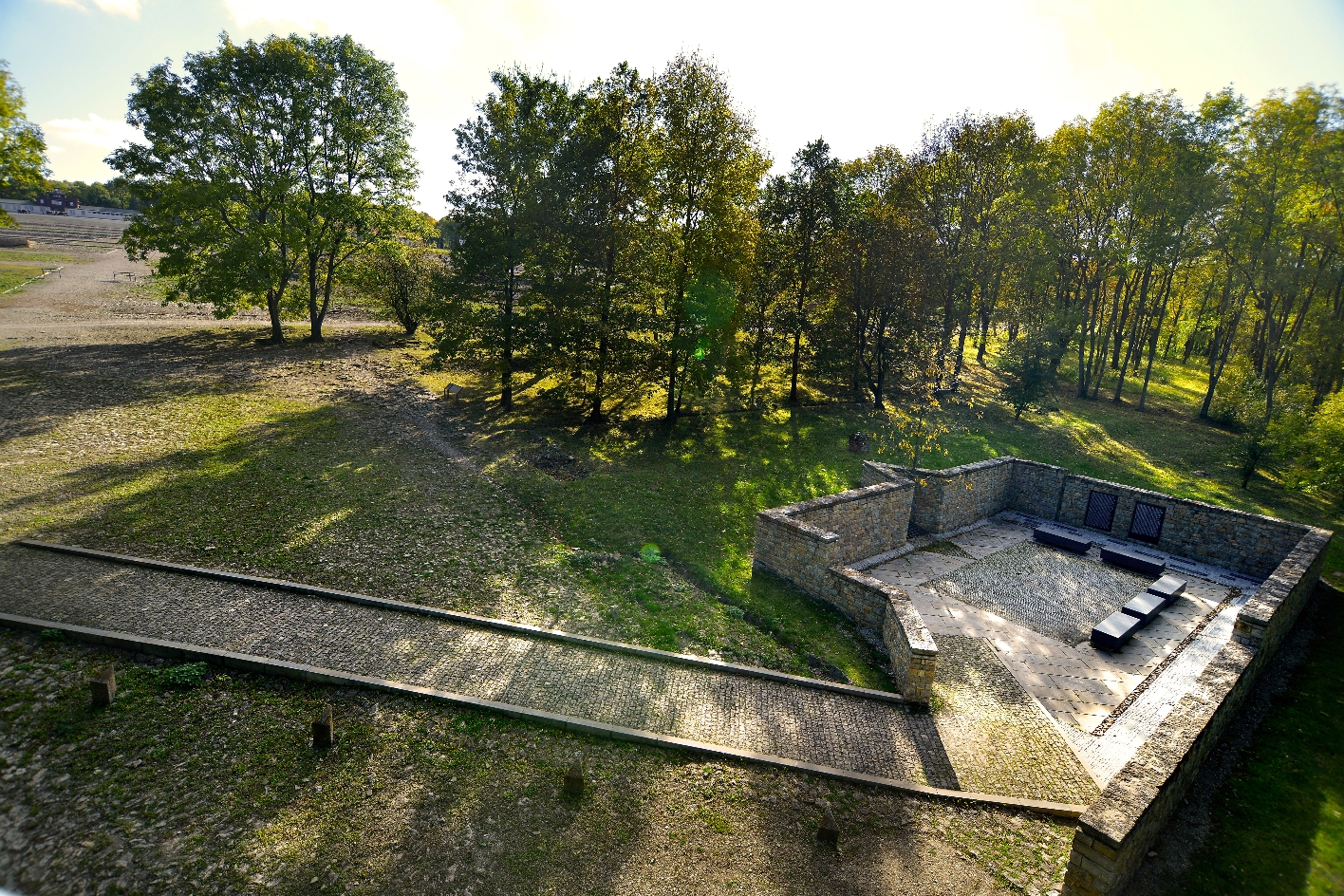 The access path leads down into a brick room without a roof. A young tree stands in a jagged recessed corner in the wall. Black stone benches.