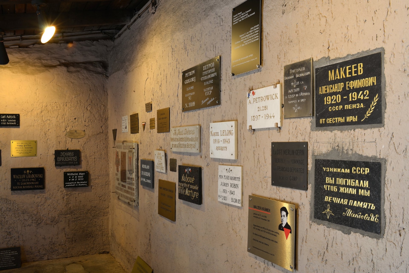 An der Wand des Gedenkraums hängen mehrere Gedenktafeln in verschiedenen Sprachen und verschiedenster Gestaltung