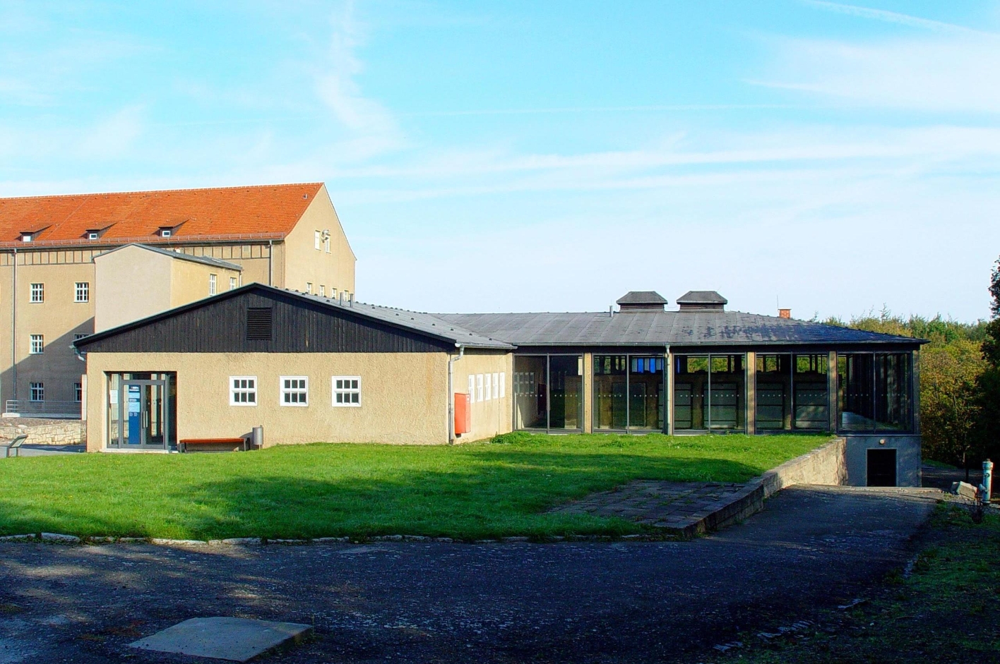 The flat former disinfection building as it looks today. The right wing has glass walls. In the background the former depot building.