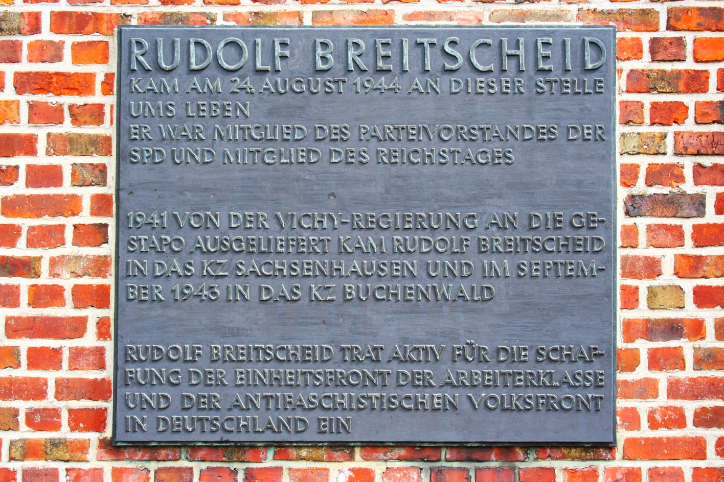 Memorial plaque for Rudolf Breitscheid on a brick wall. There it says: "Rudolf Breitscheid was killed at this spot on August 24, 1944. He was a member of the party executive of the SPD and a member of the Reichstag. Extradited to the Gestapo by the Vichy government in 1941, Rudolf Breitscheid was sent to Sachenhausen concentration camp and in September 1943 to Buchenwald concentration camp. Rudolf Breitscheid advocated the creation of the united front of the working class and the anti-fascist popular front in Germany.