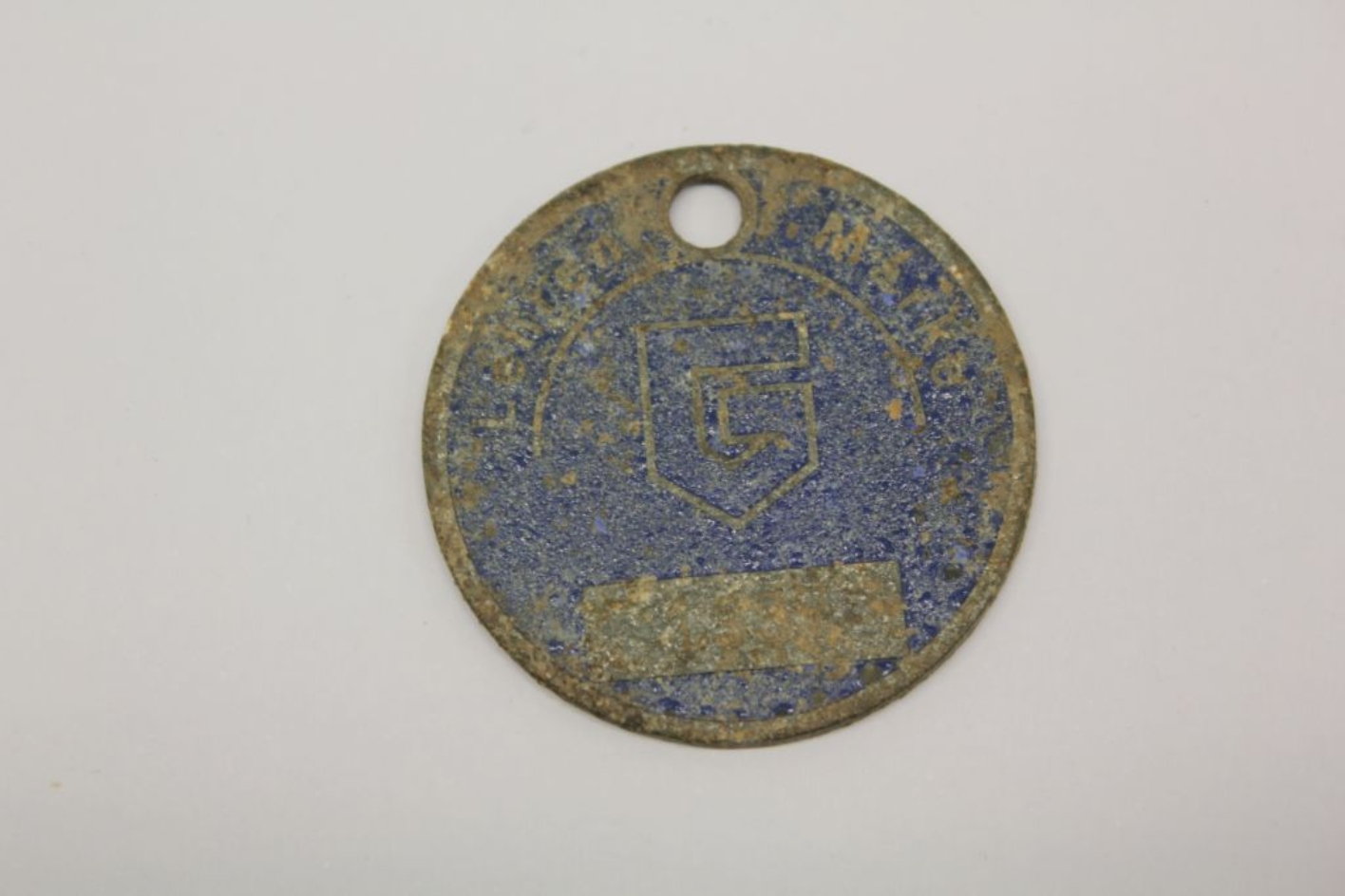 Circular mark. The front is dark blue enamel with underlined single-line lettering "Lehren Marke" arranged in a semicircle. In the center a stylized "G" as a logo. Much rust. 