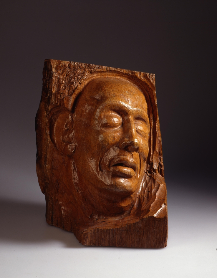A wooden sculpture depicting a face with closed eyes. 