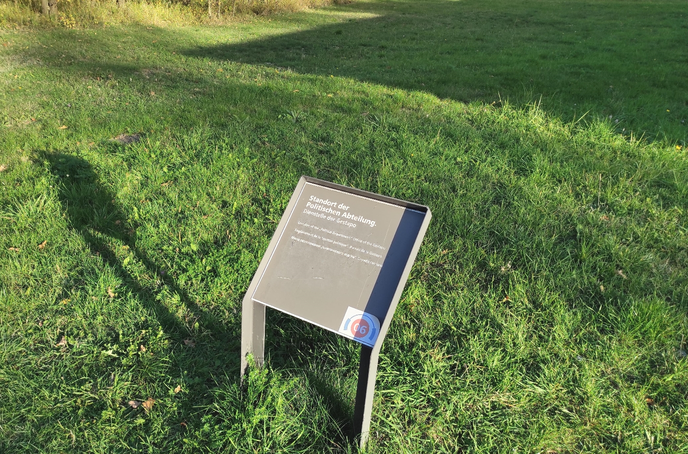 Ein Infoschild mit der Aufschrift: "Standort der Politischen Abteilung"auf einer grünen Rasenfläche.