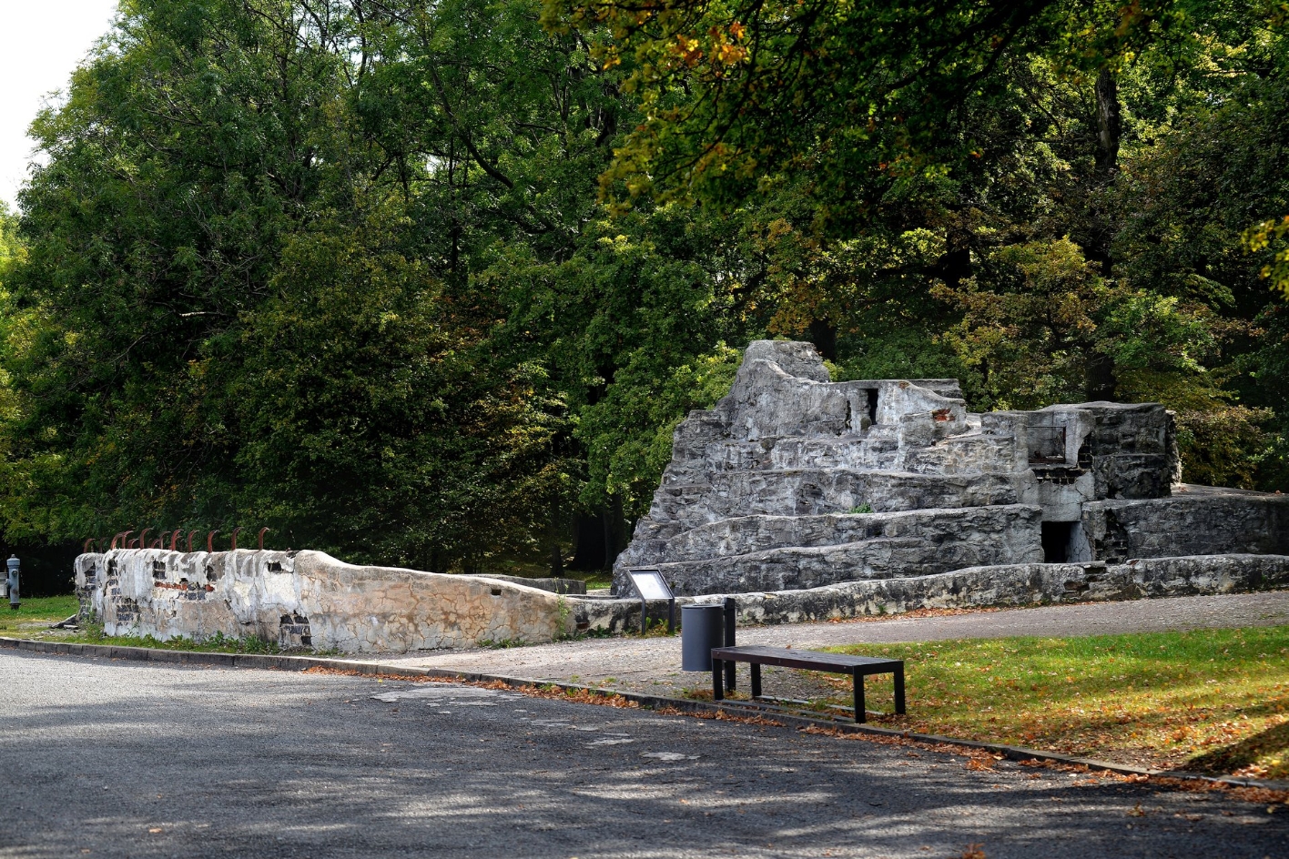 The remains of masonry of an enclosure with a rock-like structure in the middle. In front of it is an information sign. 