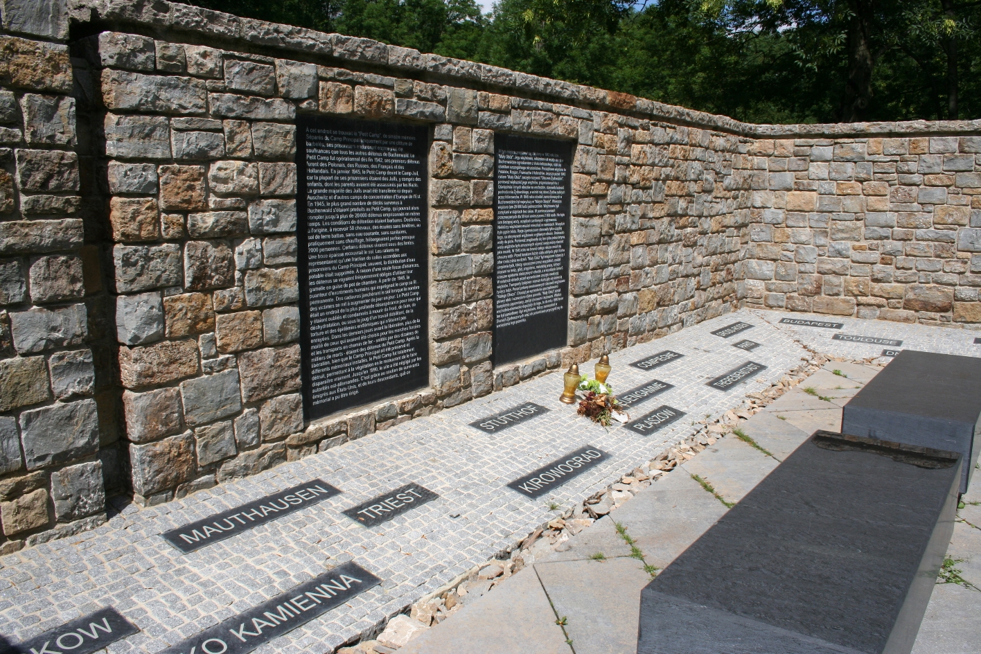 Two densely written black memorial plaques on the wall. In front of them on the floor are smaller black plaques with place names.