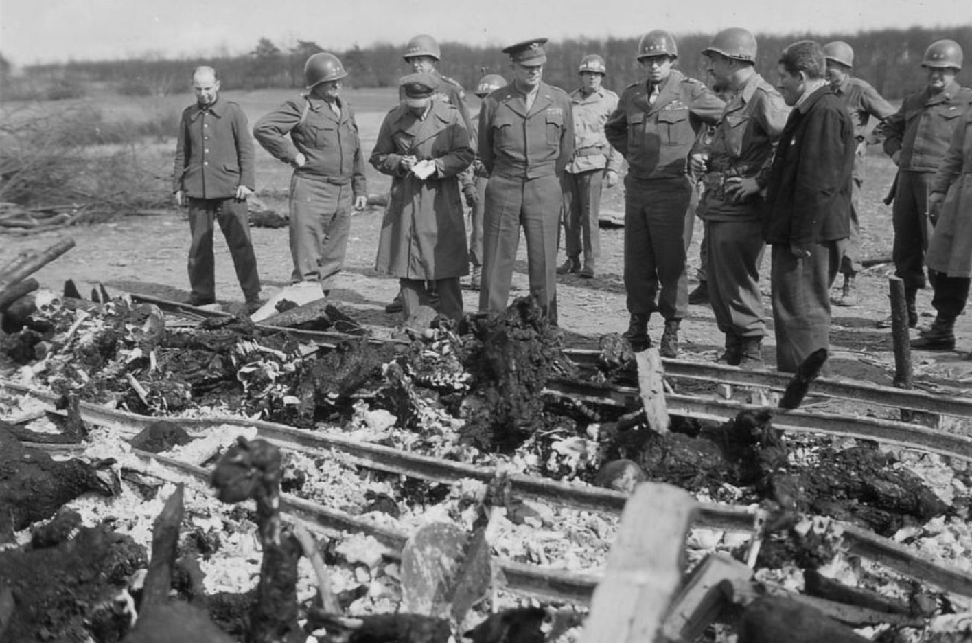 Einer der Überlebenden des Außenlagers Ohrdruf zeigt Generälen der US-Armee einen von der SS errichteten Rost aus Eisenbahnschienen, auf denen sie Häftlingsleichen verbrannten.