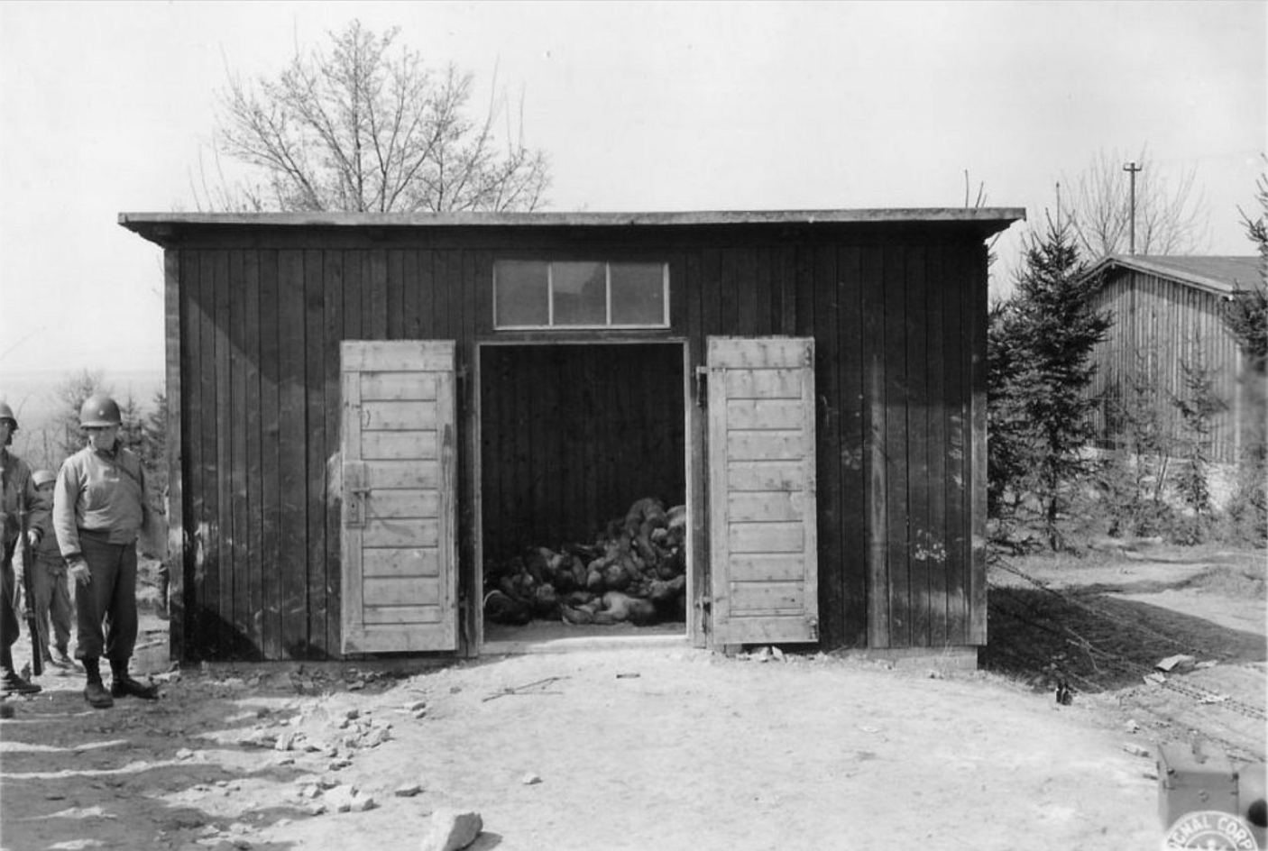 View into a barrack of the Ohrdruf subcamp, where stacked corpses of deceased prisoners lie. American soldiers are standing next to the open door.