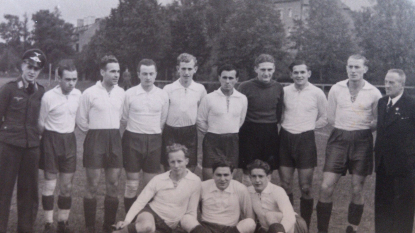 Zu sehen ist eine Fussballmannschaft in weißen Trikots. Links steht ein mann in SS-Uniform. Ganz rechts steht Fritz Förderer.