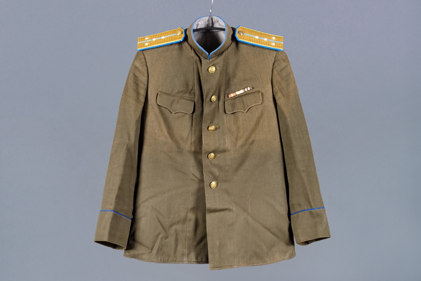 Foto einer olivgrünen Uniformjacke eines Mitarbeiters des NKWD im Range eines Hauptmannes. Auf beiden Schultern sind blaugelbe Epauletten angebracht. Die Uniform hat goldene Knöpfe.