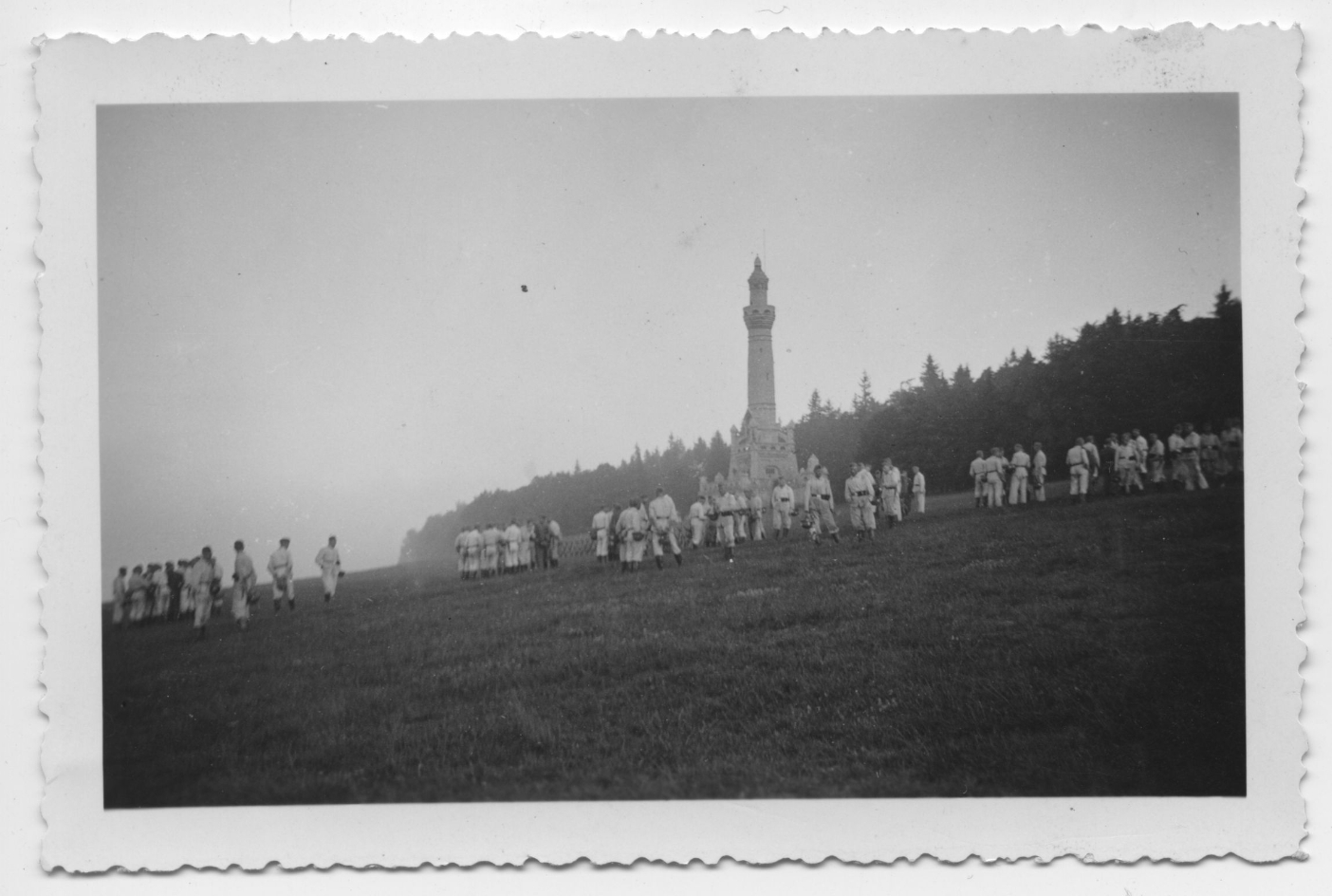 SS members of Totenkopf-Standarte 14 during a combat exercise on the southern slope of the Ettersberg. The uniformed men are standing in groups on the open meadow. The Bismarck Tower can be seen in the background.