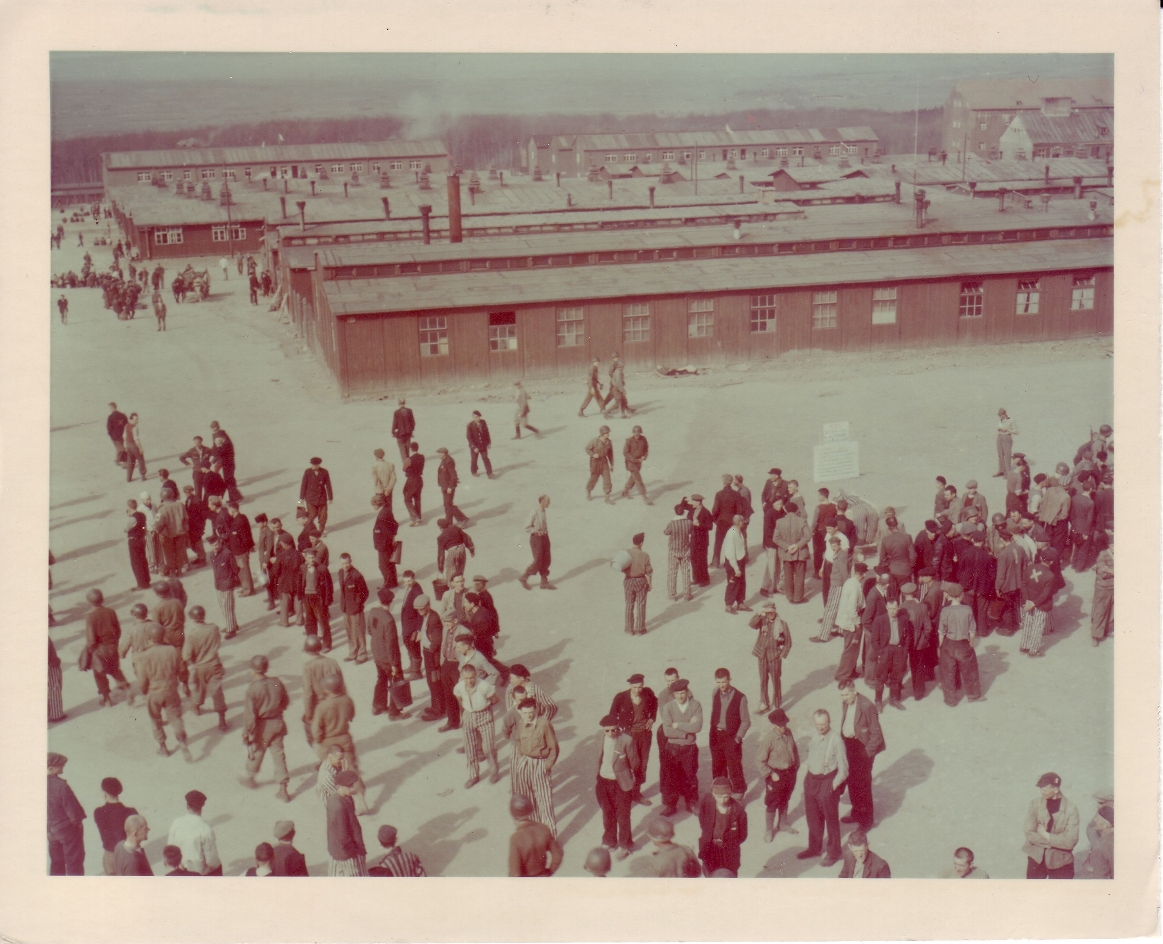 View from the gate building over the camp. Liberated prisoners and US soldiers are standing on the roll call square. The chamber building is in the far right background.