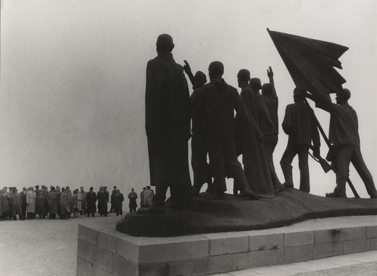 The sculpture by Fritz Cremer erected on the Platz der Freiheit can be seen in the foreground from behind. On the left side in the background is a crowd of people looking in the direction of the sculpture.