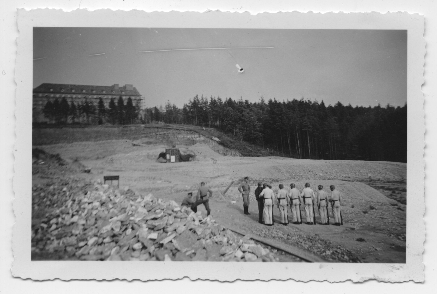 SS-Angehörige der Totenkopf-Standarte 14. Einige uniformierte Männer stehen im Steinbruch des Konzentrationslagers Buchenwald. Im Hintergrund ist die im Bau befindliche Hundertschaftskaserne Nr. 1 der Waffen-SS zu erkennen.