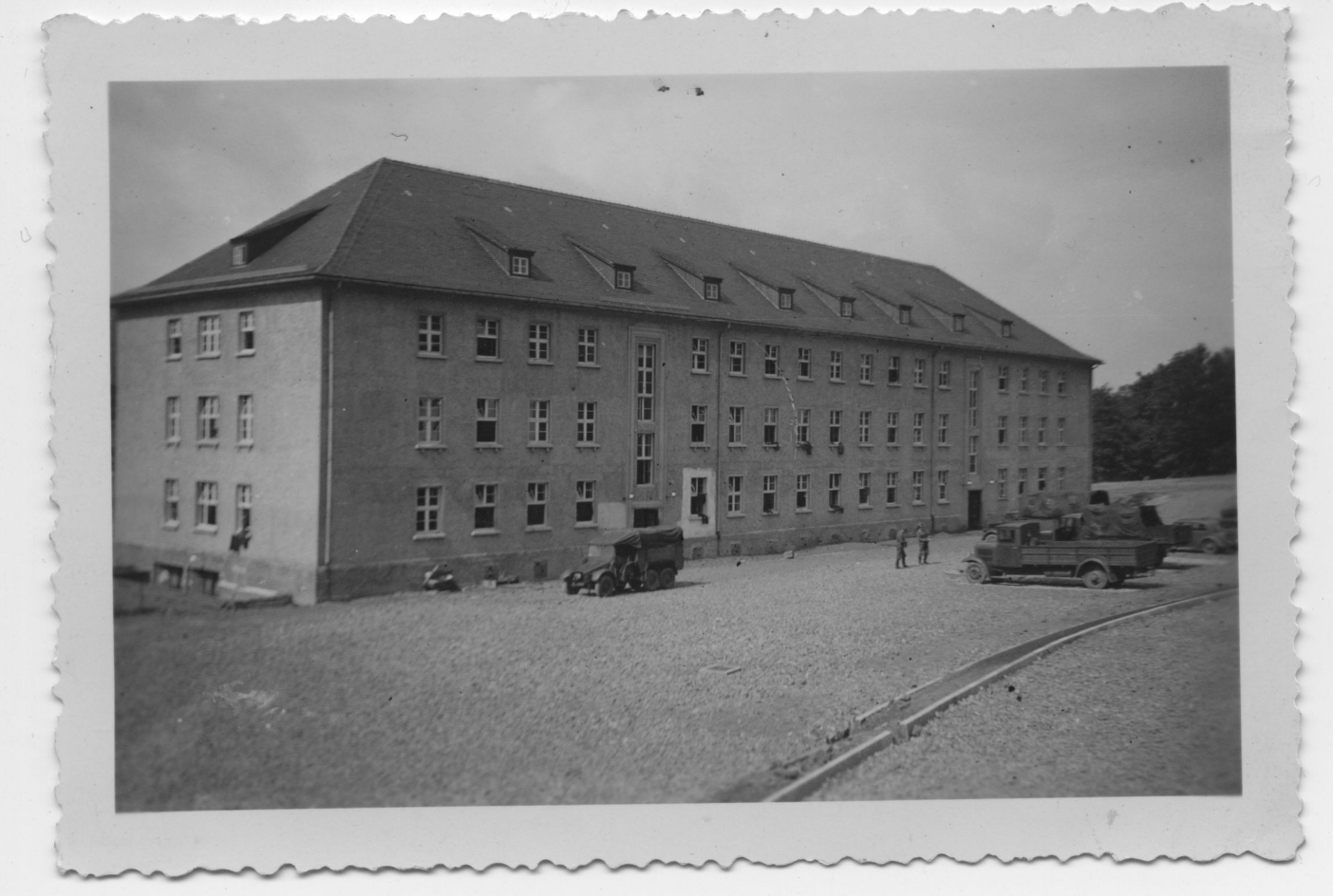 Blick auf die Hundertschaftskaserne Nr. 2 der Waffen-SS oberhalb des Steinbruchs. Vor der Kaserne parken Laster. Vereinzelnd stehen SS-Männer herum. 