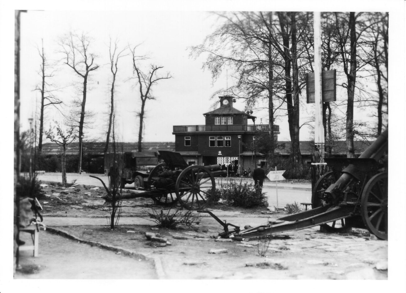 Two artillery pieces. In the background is the gate building. A small crowd is gathered in front of it. The gate is open.