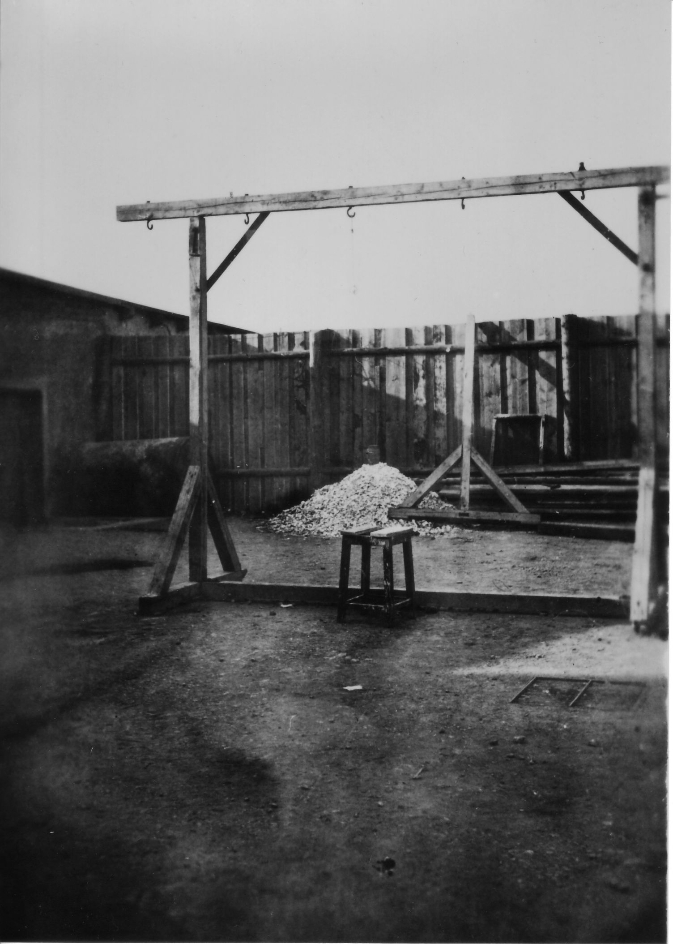 Transportabler Galgen im Innenhof des Krematorium. Im Hintergrund ist ein Aschehaufen zu sehen, in dem noch Knochenreste verbrannter Häftlinge zu erkennen sind.