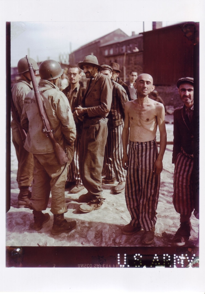 Emaciated liberated prisoners of the Small Camp talking to American soldiers. An emaciated shirtless former prisoner looks directly into the camera.