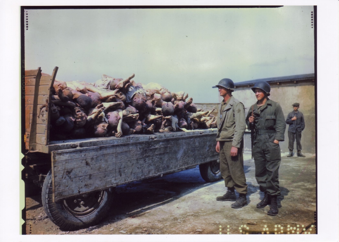 Zwei amerikanische Soldaten vor einem Anhänger mit Leichen im Innenhof des Krematoriums. Im Hintergrund ein befreiter Häftling