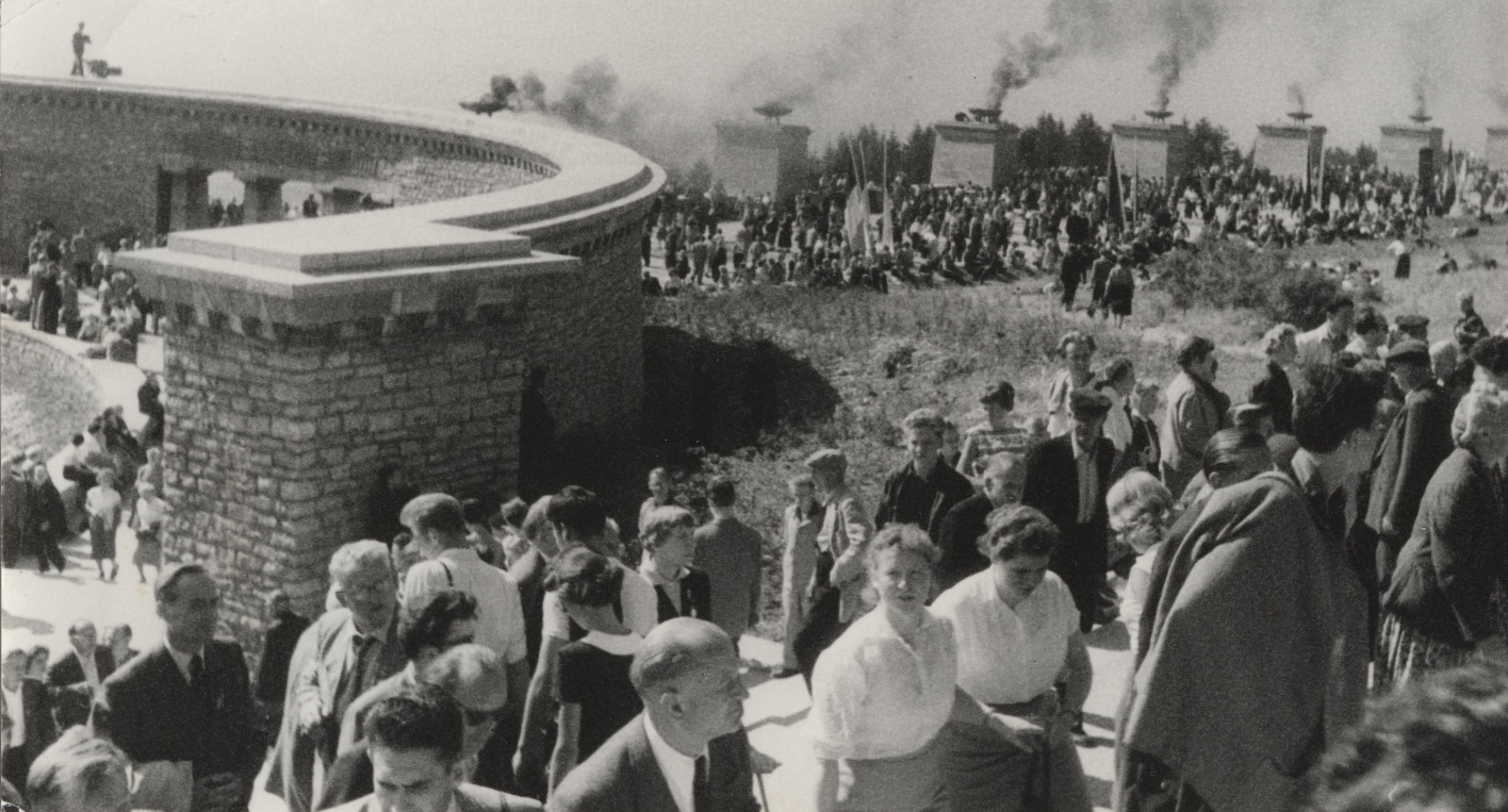 A large procession of participants of the opening ceremony of the National Memorial walks down the Street of Nations, through the one ring grave and up the stairs towards the Freedom Tower. The fire bowls on the pylons of the Street of Nations are lit.
