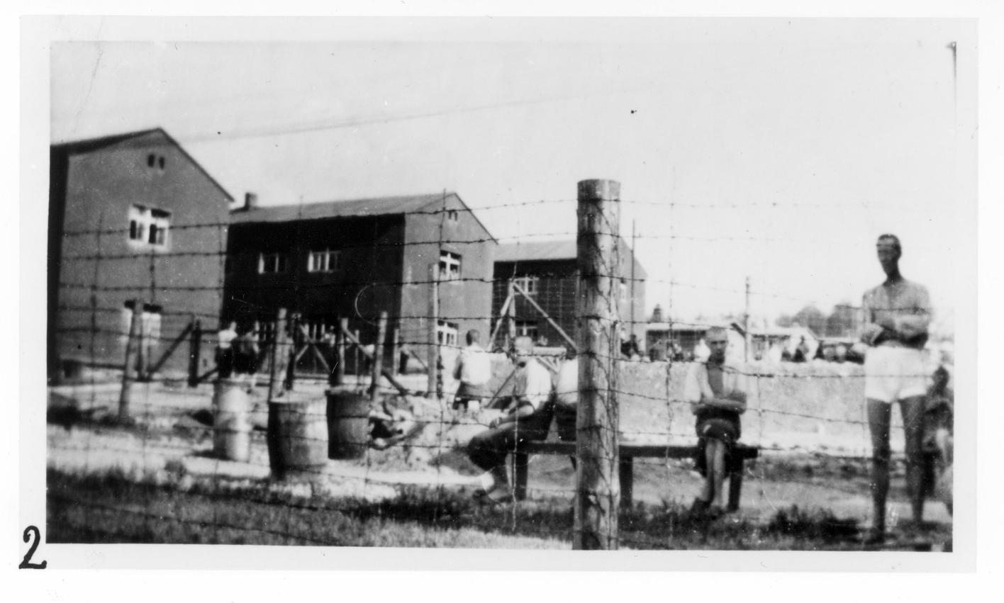Blick aus dem westlichen Randbereich des Kleinen Lagers ins Hauptlager. Im Vordergrund sitzende bzw. stehende Häftlinge. Links im Bild die Steinblocks 46, 41 und 36.