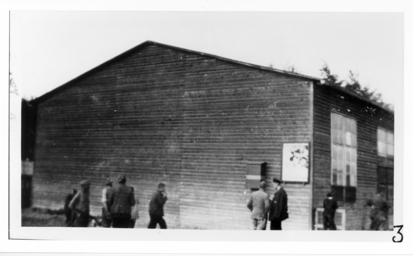 Häftlinge vor der Kinobaracke. Rechts an der Barackenwand hängt ein Filmplakat.