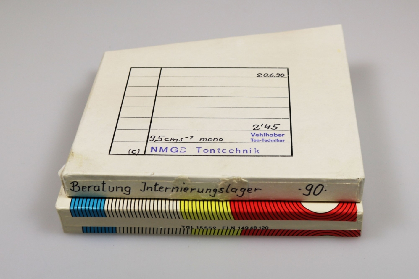 Vor einem weißen Hintergrund liegt eine zweiteilige Pappschachtel. Darauf finden sich Stempel und handschriftliche Eintragungen.