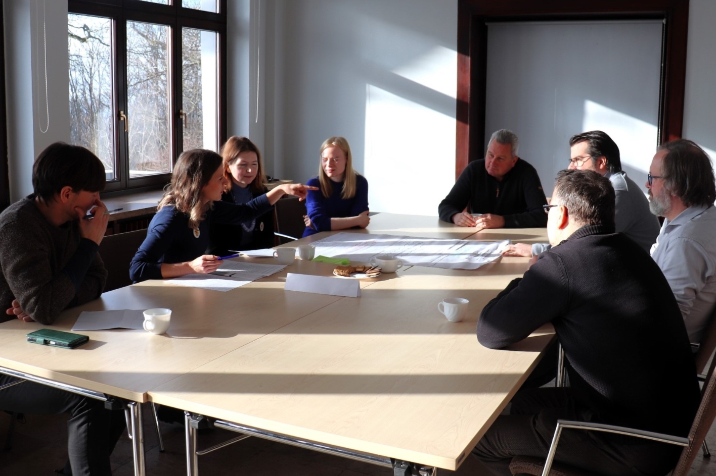 8 Personen sitzen um einen großen Tisch und diskutieren. 