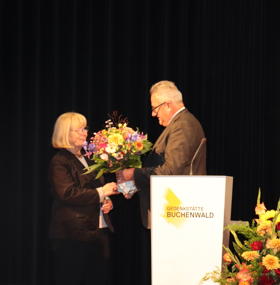 Der Direktor der Gedenkstätte Buchenwald Jens-Christian Wagner überreicht Heidrun Brauer am Rednerpult einen großen Blumenstrauß zum Dank für ihren Einsatz für die Speziallager-Erinnerung.