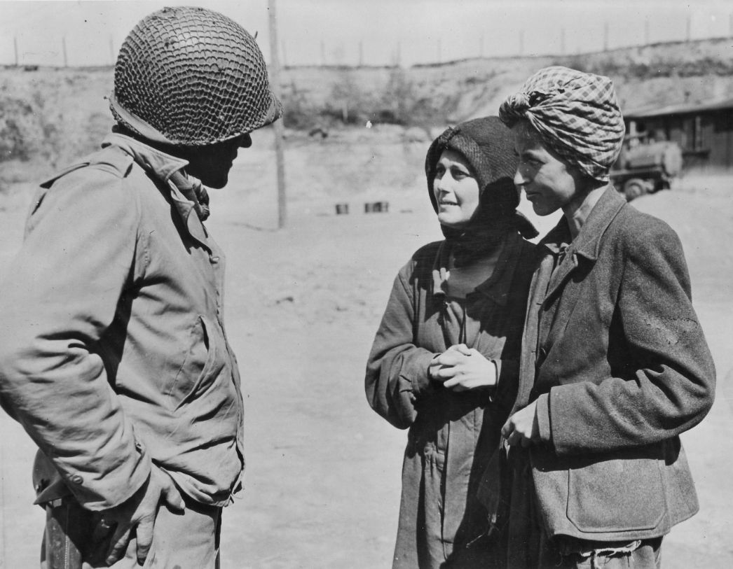 Zwei Frauen unterhalten sich mit einem amerikanischen Soldaten in Uniform und Helm. 